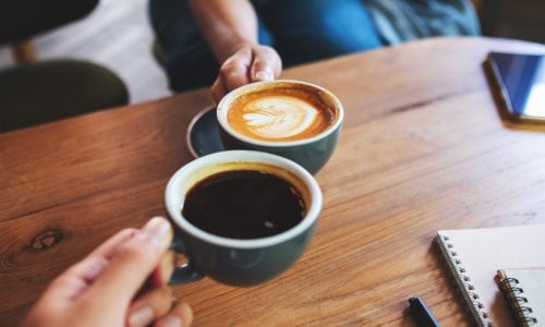 Closeup image of a man and a woman clinking coffee mugs in cafe